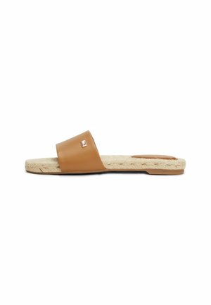 Brown slide sandal with wide leather strap, woven jute sole, and small rectangular metal logo on strap, shown in side profile.