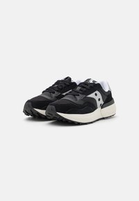 Zapatillas deportivas negras que combinan materiales de ante y malla, con una suela blanca gruesa y sutiles acentos grises en los paneles laterales.