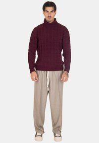 Maglione a collo alto in maglia grossa color bordeaux, con polsini e orlo a costine, abbinato a pantaloni palazzo grigi chiari e sneakers bianche con dettagli neri.