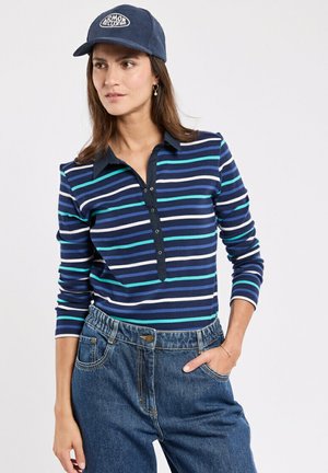 Haut à rayures bleu marine et blanc à manches longues avec un col et une patte de boutonnage, associé à un pantalon en denim bleu taille haute.