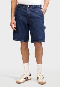 Denimshorts med mørkeblå vask, avslappet passform og sidelommer. Kjørt med hvite sokker og retro-stil joggesko.