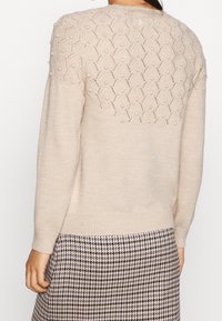 Beige gebreide trui met een gestructureerde, patroon achter yoke met verhoogde accenten, lange mouwen en een geribde zoom. Draag over een geruit rokje.