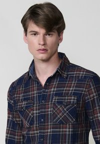 Camicia a quadri blu navy e bordeaux con maniche lunghe, chiusura a bottoni sul davanti, due tasche sul petto e colletto classico, realizzata in tessuto intrecciato.