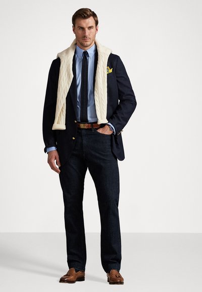Marine blazer med gullknapper, lyseblå skjorte, strikket kremhalskjede, mørk denimjeans, brune skinnsko. Enkelt og klassisk design.