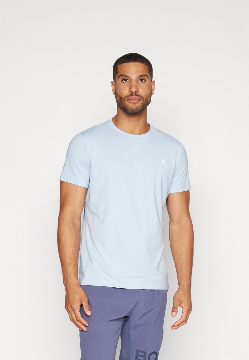 Camiseta de manga corta azul claro con cuello redondo, hecha de tela suave; presenta un pequeño logo en el lado izquierdo del pecho.