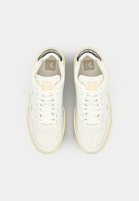 Sneakers bianchi in pelle con punta perforata, dettagli grigi, suola gialla e lacci. Presentano un logo sulla linguetta e sui lati.