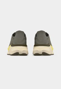 Ζευγάρι γκρι και κίτρινων αθλητικών παπουτσιών, που φαίνονται από πίσω, με ανάγλυφη φτέρνα και παχιές εκρού σόλες σε απλό φόντο.