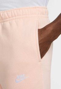 Pantalones de chándal rosa claro hechos de una tela suave, con cintura elástica y bolsillo lateral; logo de Nike blanco bordado en la parte delantera.