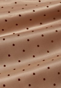 Jasnobrązowa tkanina z małymi, równomiernie rozmieszczonymi ciemnobrązowymi kropkami i widoczną strukturą splotu, pokazana w miękkich falach.