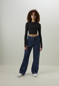 Top cropped preto de mangas longas com um design ajustado, combinado com calças largas de ganga azul tipo cargo com múltipos bolsos. Ténis brancos completam o visual.