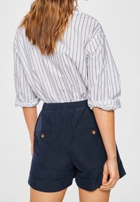 Námořnické modré šortky s vysokým pasem, které mají dvě zadní kapsy a zlaté knoflíky. V kombinaci s bílou pruhovanou blůzkou.