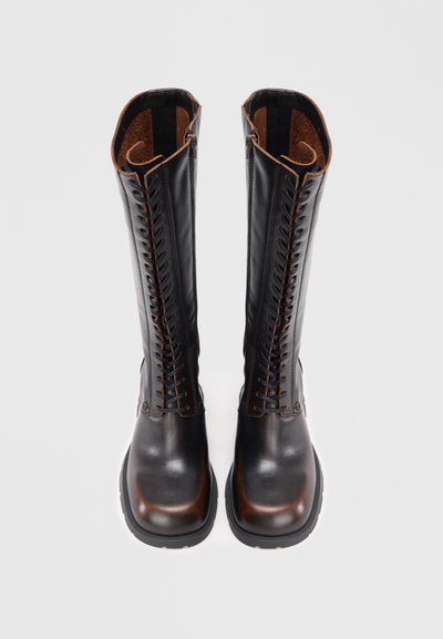 Fekete bőrből készült térdig érő csizma barna részletekkel, elöl fűzős, sima, fényes felülettel és masszív fekete talppal.