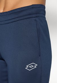 Jūreivių sportiniai kelnių pagaminti iš lygios, tamprios medžiagos. Yra dvigubai siūti juosmens kraštai ir balta logotipo aplikacija ant šlaunies.