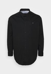 Chemise noire à manches longues avec boutons, col pointu et petit logo blanc "CK" sur la poitrine gauche.