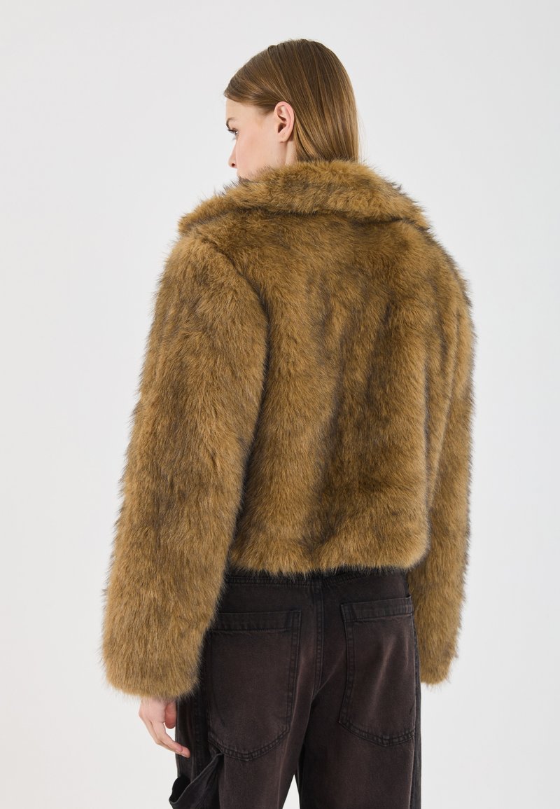 Giacca in pelliccia sintetica marrone con colletto, design cropped e maniche lunghe, abbinata a pantaloni scuri, che mette in evidenza una finitura morbida e texturizzata.