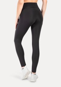 Czarne legginsy z wysokim stanem, wykonane z elastycznego materiału, dopasowane w nogawkach, zestawione z białymi butami sportowymi z czarnymi akcentami.