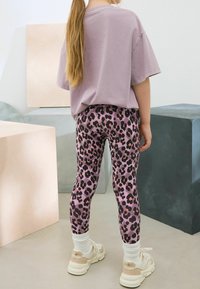 Lila bomullströja matchad med rosa leopardmönstrade leggings. Outfiten har vita ribbade strumpor och krämfärgade sneakers för en avslappnad look.