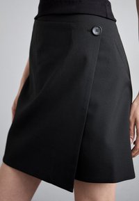 Juoda suvyniota sijonas, pagamintas iš lygios medžiagos, su vienu juodu mygtuku juosmens srityje ir švariu apvadu be papildomų raštų.