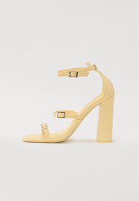 Yellow block-heeled sandals with three adjustable straps, square toe design, smooth synthetic material, and silver-tone buckles.