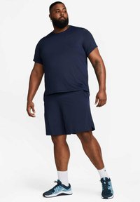Navy athletic outfit consisting of a short-sleeve shirt and shorts, featuring a smooth texture. Paired with blue and black sneakers.