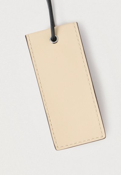 Étiquette à bagage rectangulaire en cuir beige avec des bords cousus et une sangle noire passant à travers un œillet métallique en haut.