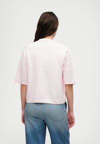 Korte mouwen, cropped sweater in zachtroze stof met een gestructureerde afwerking. Heeft een ronde halslijn en een enkele gestikte zoom. Gemaakt in combinatie met blauwe jeans.
