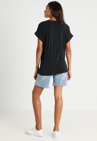 Black, relaxed-fit t-shirt with rolled sleeves, paired with light blue denim shorts and white sneakers, viewed from the back.