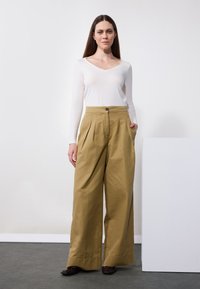 Long-sleeve white top with a V-neck paired with high-waisted, wide-legged khaki pants featuring pleats and side pockets.