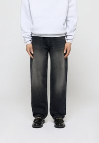 Jeans de pierna ancha de lavado oscuro con un acabado descolorido, que cuentan con un diseño clásico de cinco bolsillos. Combinados con una sudadera gris claro y zapatos negros.