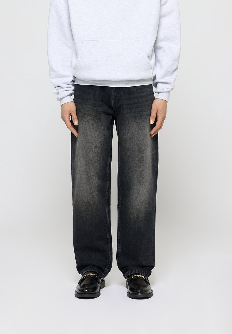 Jeans de pierna ancha de lavado oscuro con un acabado descolorido, que cuentan con un diseño clásico de cinco bolsillos. Combinados con una sudadera gris claro y zapatos negros.