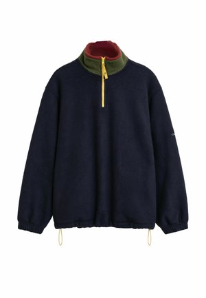 Pull en polaire navy avec un col haut, doté d'une doublure intérieure verte et d'une fermeture éclair jaune. Manches élastiques et un détail avec cordon de serrage à l'ourlet.