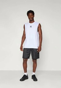 Valge ilma varrukateta tank top musta logoga, koos mustade võrguliste lühikeste pükstega. Jalanõud on mustad ja sokid valged. Lihtne, sportlik disain.