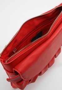 Rød lædertaske med en tekstureret, sammensat design. Har en guldlynlås og rød foring med en lille indvendig lomme til organisering.