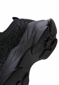 Black athletic shoe with a textured upper, a cushioned heel, and a patterned rubber sole featuring ridges and a star shape for traction.