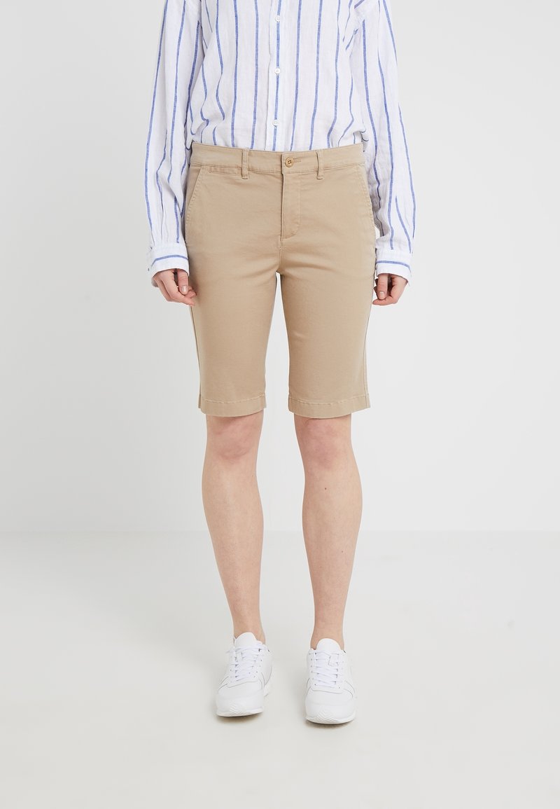 Beige šortky ke kolenům vyrobené z bavlny, mají rovný střih, boční kapsy, poutka na pásek a ohrnutý lem. Kombinováno s modro-pruhovanou košilí.