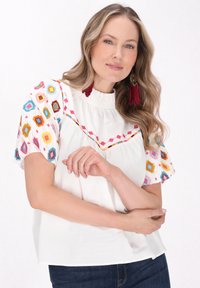 Biała bawełniana bluzka z kolorowym, geometrycznym haftem na krótkich rękawach, z falbaniastym dekoltem i luźnym krojem.