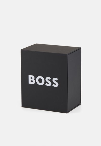Boîte en carton noire avec un logo "BOSS" blanc sur le devant. Forme rectangulaire, texture lisse, design épuré sans détails supplémentaires.