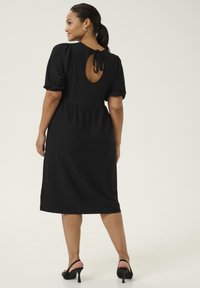 Zwarte jurk tot de knie met pofmouwen, met een sleutelgatontwerp aan de achterkant en striksluiting. Gladde textuur, eenvoudige silhouet en minimale accenten.