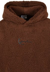 Rudos fliso džemperis su tekstūruotu paviršiumi, turintis priekinius kišenę ir juodą logotipo siuvinėjimą ant krūtinės. Su kapuci.