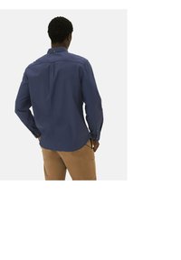 Marinblå skjorta med knappar, lång ärm, ryggveck och rundad nederkant, tillverkad av ett mjukt tyg. Kombinerad med beige byxor.