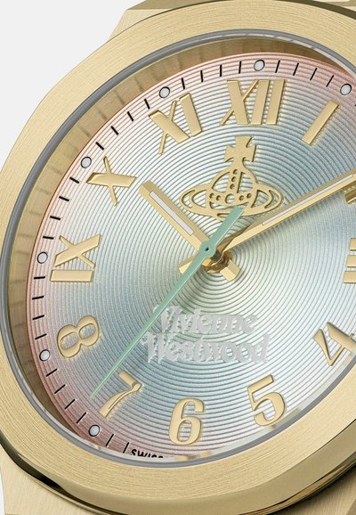 Goudkleurige klok met Romeinse en Arabische cijfers, een kroonembleem op 12 uur en het "Vivienne Westwood" logo boven de positie van 6 uur.