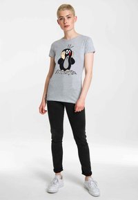 Gray t-shirt with a graphic of a cartoon mole, black and white with red accents, paired with black pants and white sneakers.