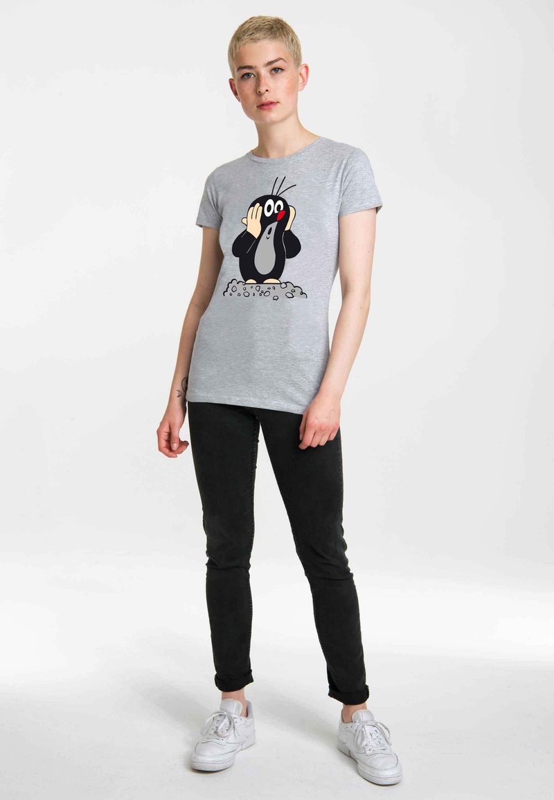 Gray t-shirt with a graphic of a cartoon mole, black and white with red accents, paired with black pants and white sneakers.