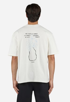 T-shirt en coton blanc à la coupe décontractée. Le dos présente un graphisme d'un vase avec des fleurs et du texte en noir, dans un style de dessin linéaire minimaliste.