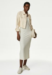 Giacca in denim beige cropped sopra un abito midi a coste grigio chiaro, abbinata a sneakers avorio e una piccola borsa.