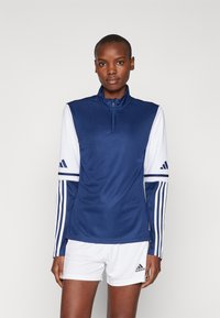 Marine athletic top med høj krave, lynlås lukning og hvide ærmer med tre striber og logo. Glat tekstur, designet til sport.