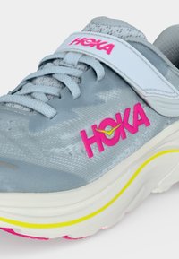 Γκρι παπούτσι τρεξίματος Hoka με ροζ λογότυπο, λευκό ιμάντα και κίτρινη διακοσμητική γραμμή στη χοντρή λευκή σόλα.