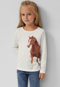 Langärmliges weißes Baumwollhemd mit einem bedruckten braunen Pferd und einer detaillierten Mähne, kombiniert mit blauen Jeans.
