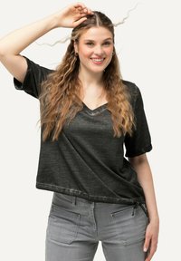 Zwart, kortwijd T-shirt met V-hals en een ontspannen pasvorm, gemaakt van iets textiel stof, gecombineerd met grijze slim-fit jeans met zakken.