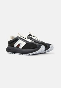 Sneakers con una toma superiore in rete nera, accenti bianchi e una suola in gomma texturizzata. Presentano una punta rotonda e lacci a contrasto.